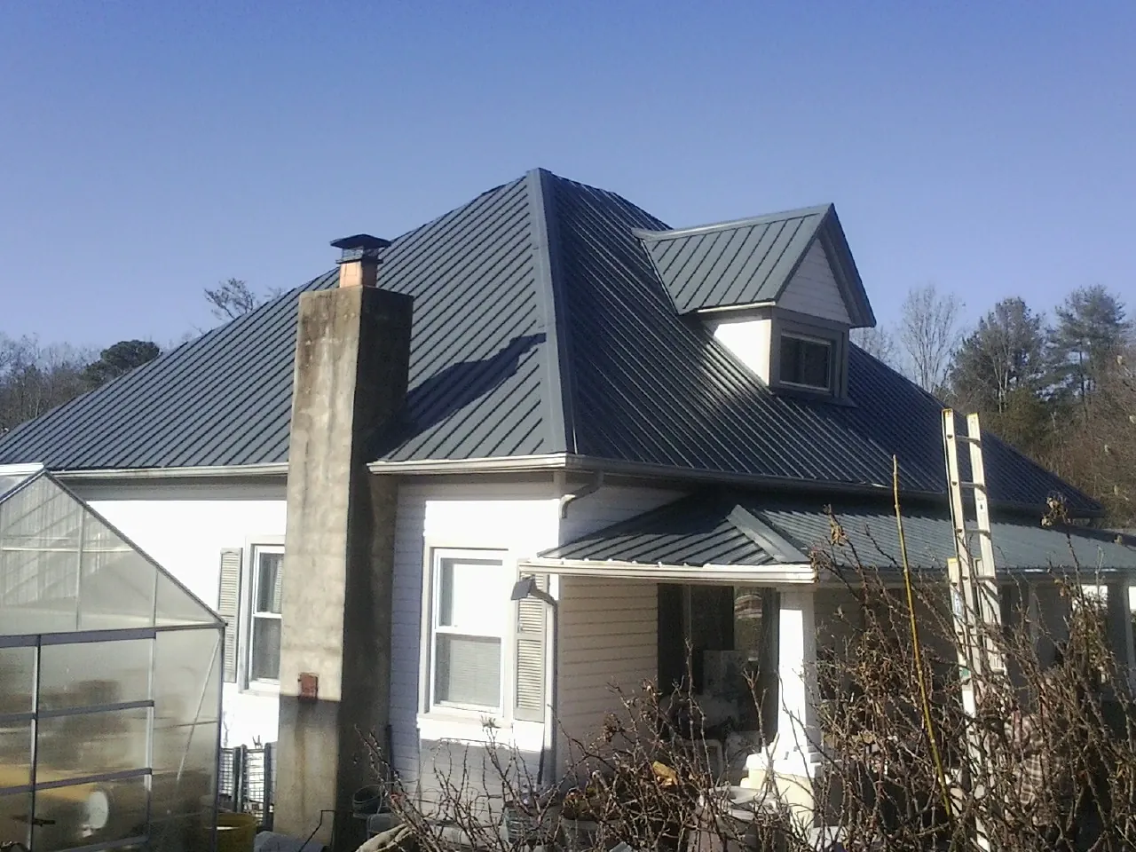 Dark blue standing seam metal roof on a white farmhouse with dormer — Slate & Tile Roof Repair by Roofing Brothers in Markle