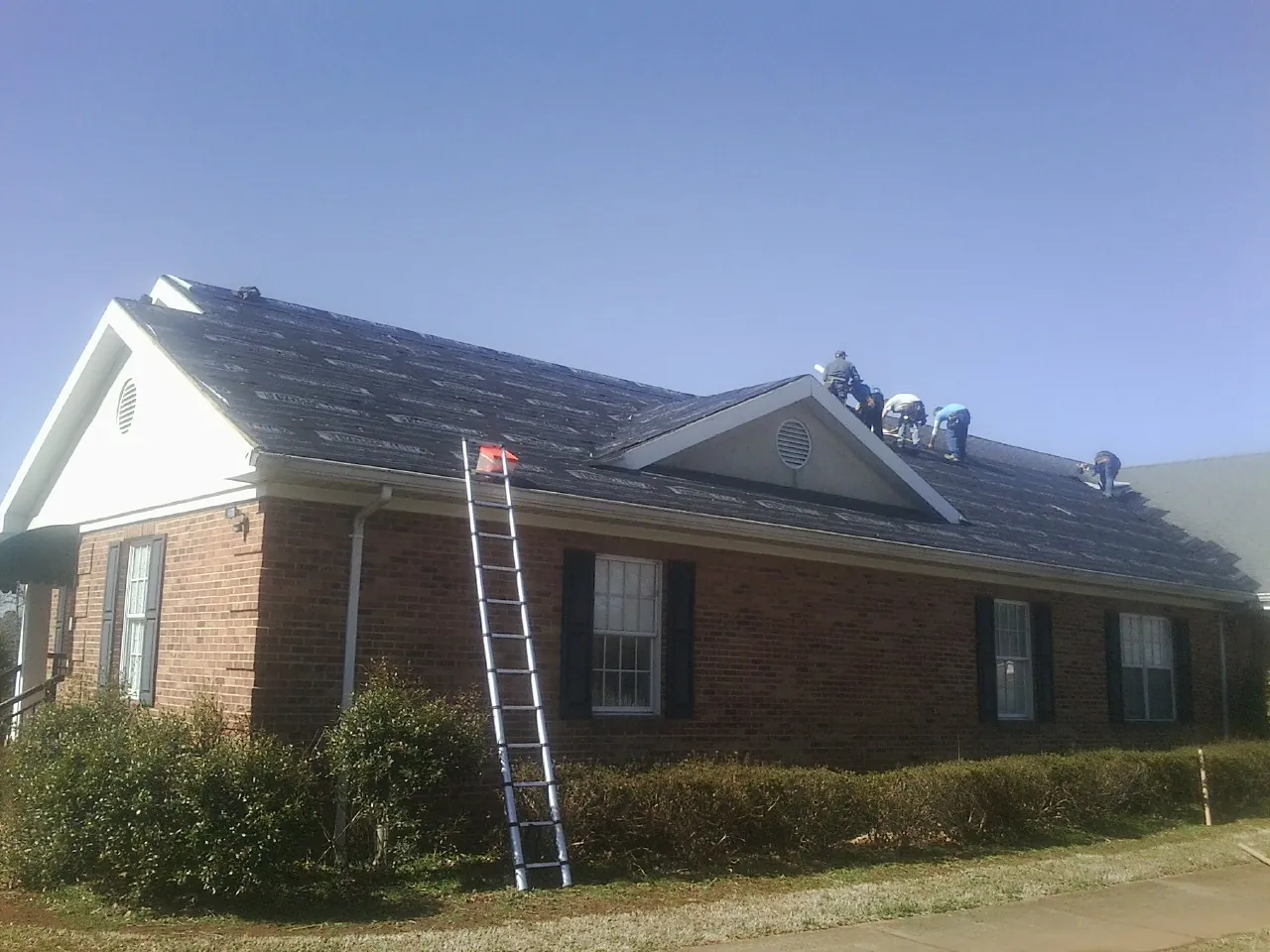 Crew tearing shingles off a brick ranch roof with a ladder set — Emergency Roof Repair work by our crew in Markle