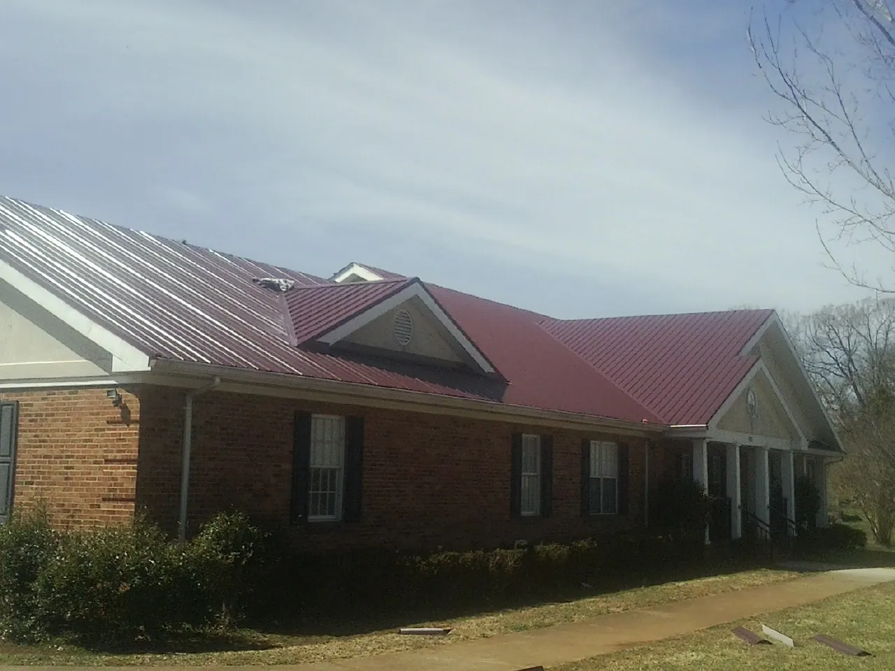 Red metal roof with gabled entries on a long brick building, from a Hail Damage Roof Repair job in Markle