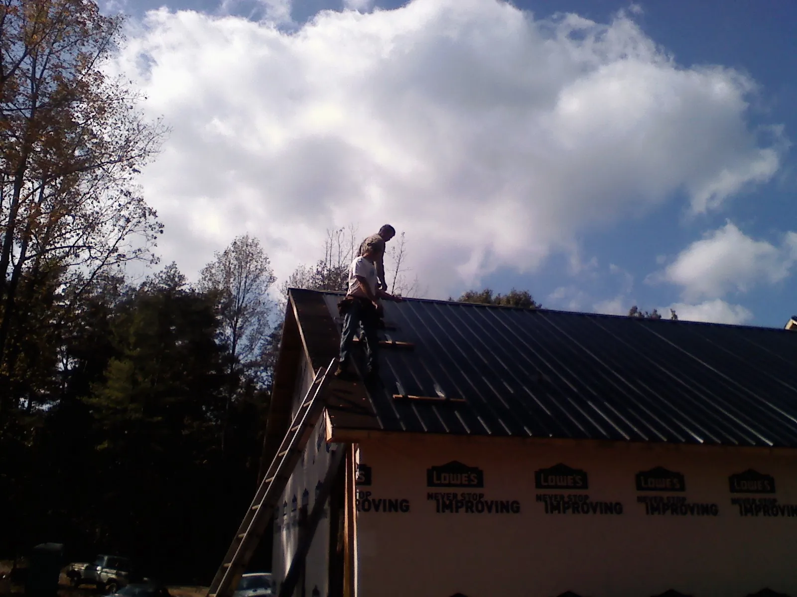 Roofer fastening dark metal panels high against a cloudy sky, from a Roof Inspection job in Markle